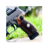 A pistol grip replacement with a dark brown wood grain body, textured black grip panels, two circular cutouts, and a silver legion logo medallion in the center.