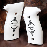 Two white grip covers with black ornate scrollwork and the text 'Durmus Eren' printed on them, displayed against a dark brown wood and leather background.