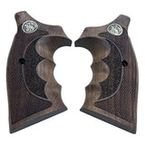 A pair of dark brown wooden pistol grips with textured checkering, a central recessed grip panel, and a silver circular metal emblem near the top, shown on a plain white background.