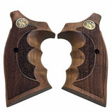 A pair of dark brown wooden pistol grips with textured checkering, featuring a gold-toned circular emblem near the top and a central recessed grip panel, shown on a plain white background.